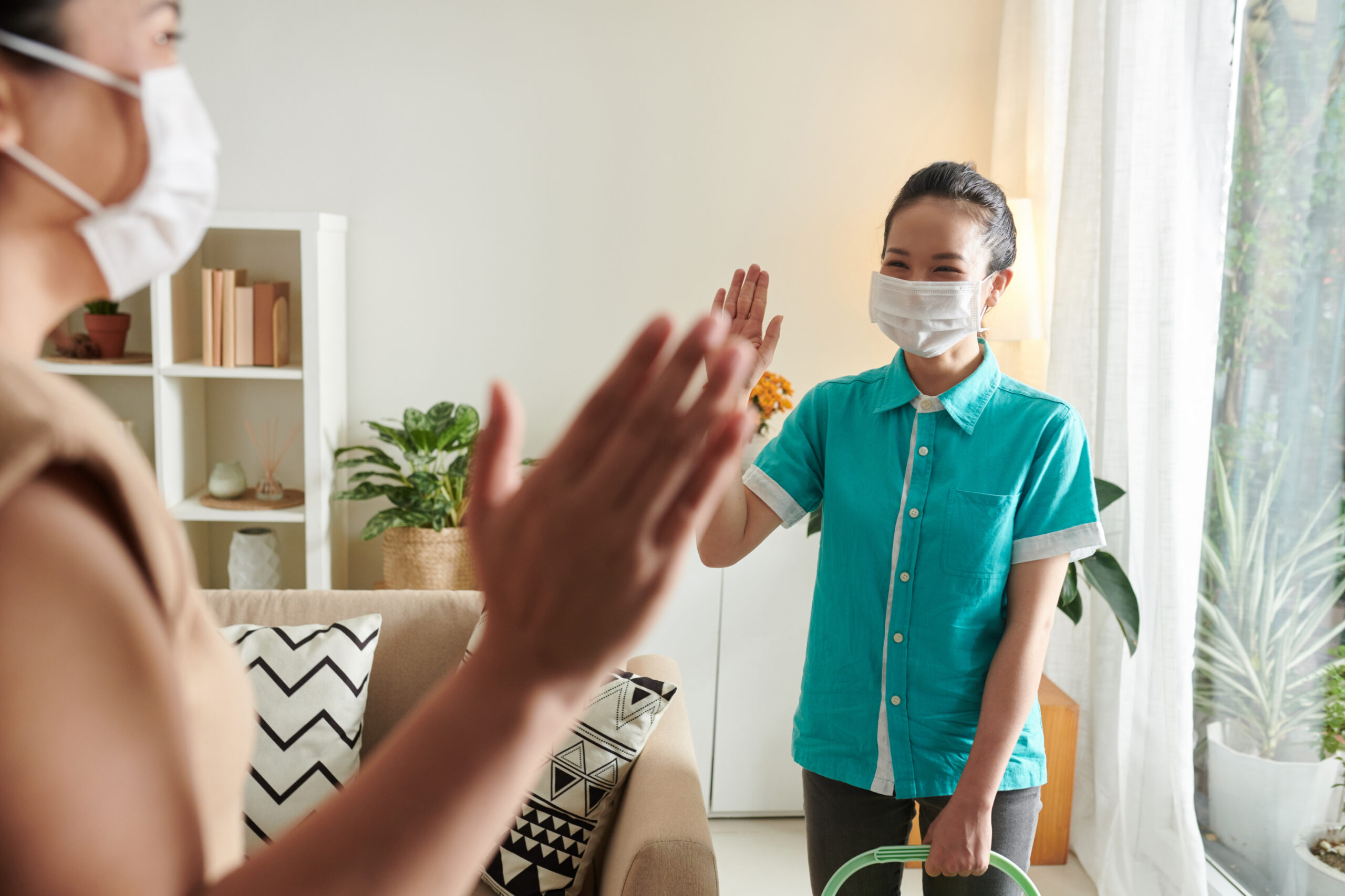 Young cleaning worker in mask waving her hand to greet the client while coming to apartment for housework